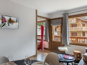 Een moderne kamer met een schilderij met ski-thema, een eethoek met een tafel en stoelen, en uitzicht op een houten gebouw met balkons.