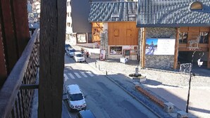Vista da rua com carros estacionados na lateral, um edifício com telhado azul e uma placa.