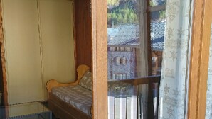 Um quarto com uma cama, um guarda-roupa de madeira e uma varanda com guarda-corpo.