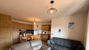 A modern living room with a leather sofa, a dark grey couch, and a wooden coffee table. There is a dining area with wooden chairs and a table, and a kitchen with wooden cabinets and appliances. - New 3-room apartment, 6 guests, terrace, parking, Les Saisies (Villard-sur-Doron)