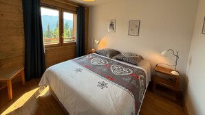 A bedroom with a bed, a desk, a chair, a window with curtains, a hanging lamp, and framed pictures on the wall. - New 3-room apartment, 6 guests, terrace, parking, Les Saisies (Villard-sur-Doron)