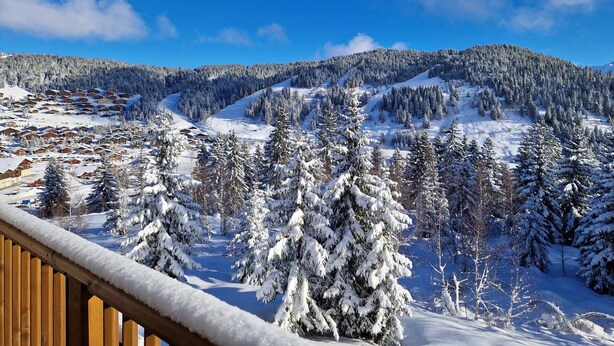A snowy mountain landscape with a wooden deck overlooking a snow-covered village and forest. - New 3-room apartment, 6 guests, terrace, parking, Les Saisies (Villard-sur-Doron)