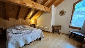Una habitación acogedora con techo de madera, una cama con colcha, una mesita pequeña y una ventana con vistas.