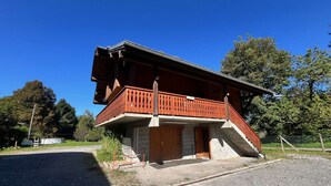 Un edificio de madera de dos pisos con un balcón y una escalera que conduce al nivel superior, además de un camino de entrada de grava.
