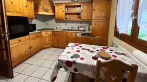 Una cocina con armarios de madera, salpicadero de azulejos, horno negro, microondas, fregadero y una mesa con mantel estampado.