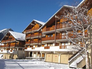 Un hotel de varios pisos con balcones de madera, suelo cubierto de nieve y montañas al fondo.
