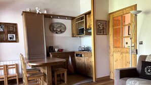 Eine gemütliche Küche mit Holzschränken, einem Esstisch und Stühlen. Im Wohnbereich befindet sich eine Couch mit einem Zierkissen.