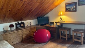 Ein gemütliches Dachzimmer mit Holzbalken, einem Fernseher, einem Schreibtisch mit Lampe und einem roten Sitzsack.