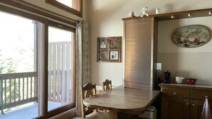 Eine gemütliche Küche mit Holztisch und Stühlen, einer Schiebetür zum Balkon und einem an der Wand befestigten Regal mit Küchenutensilien.