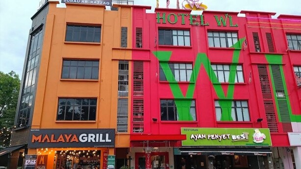 Un hotel con un llamativo letrero 'HOTEL WL', un restaurante 'MALAYA GRILL' y un restaurante 'AYAM PENYET BEST'.