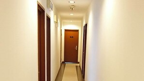 Un largo pasillo de hotel estrecho, con suelo de baldosas, puertas de madera y un letrero que indica la dirección al ascensor.
