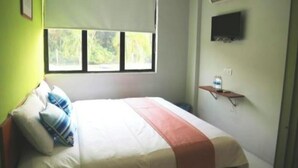 Un dormitorio con una cama, ventana, aire acondicionado y televisor en la pared.