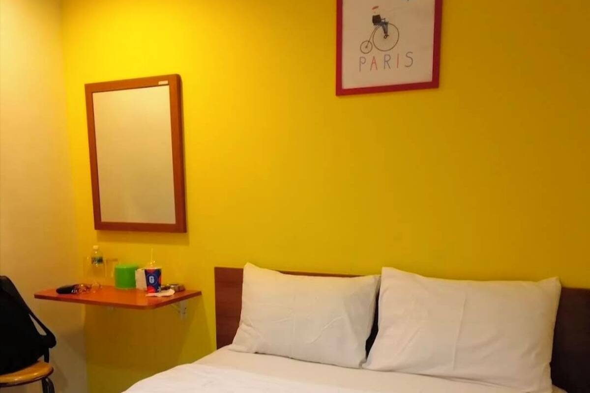 A hotel room with a bed, a bedside table with a mirror, and a wall-mounted picture of a bicycle with the word "PARIS".