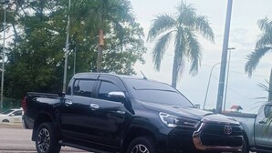 Una camioneta Toyota negra estacionada en un área pavimentada, con palmeras al fondo.
