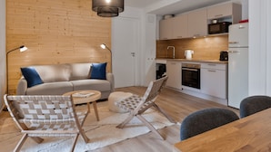 A compact living space with a sofa, two woven chairs, a small table, a kitchen area with a microwave, oven, and refrigerator. - New Apartment with Garden and Terrace near the Village (Le Monêtier-les-Bains)