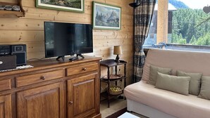 A wooden-paneled room with a television, a small table with a lamp, a sofa, and two framed landscape paintings on the wall.