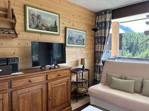 A wooden-paneled room with a television, a small table with a lamp, a sofa, and two framed landscape paintings on the wall. - Cozy Apartment, 2 Bedrooms, Montgenèvre (Montgenèvre)
