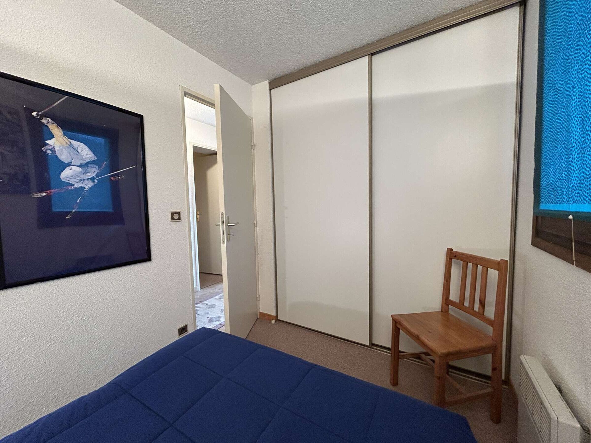Une chambre à coucher avec un lit, une chaise en bois, une armoire et un tableau encadré accroché au mur.