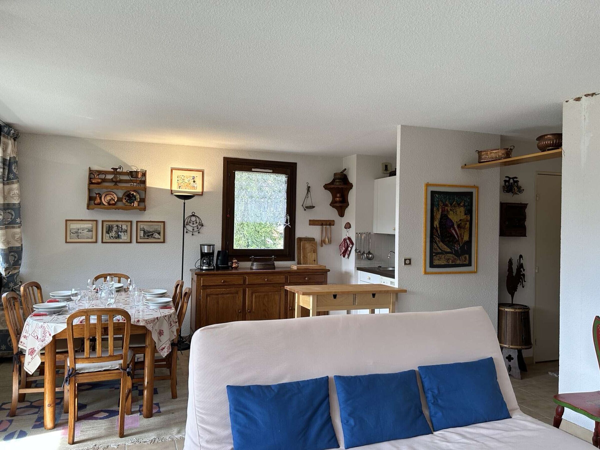 Ein gemütliches Wohnzimmer mit einer Couch, einem Esstisch für vier Personen und einer Küchenzeile mit Schränken und einem Fenster.