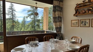 A dining area with a table set for four, a view of trees and mountains through a window, and a shelf with copper pots.