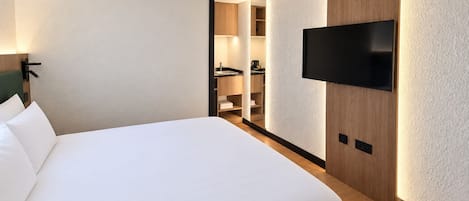 Una habitación de hotel con una cama grande, un televisor montado en la pared y un vestidor con estantes.