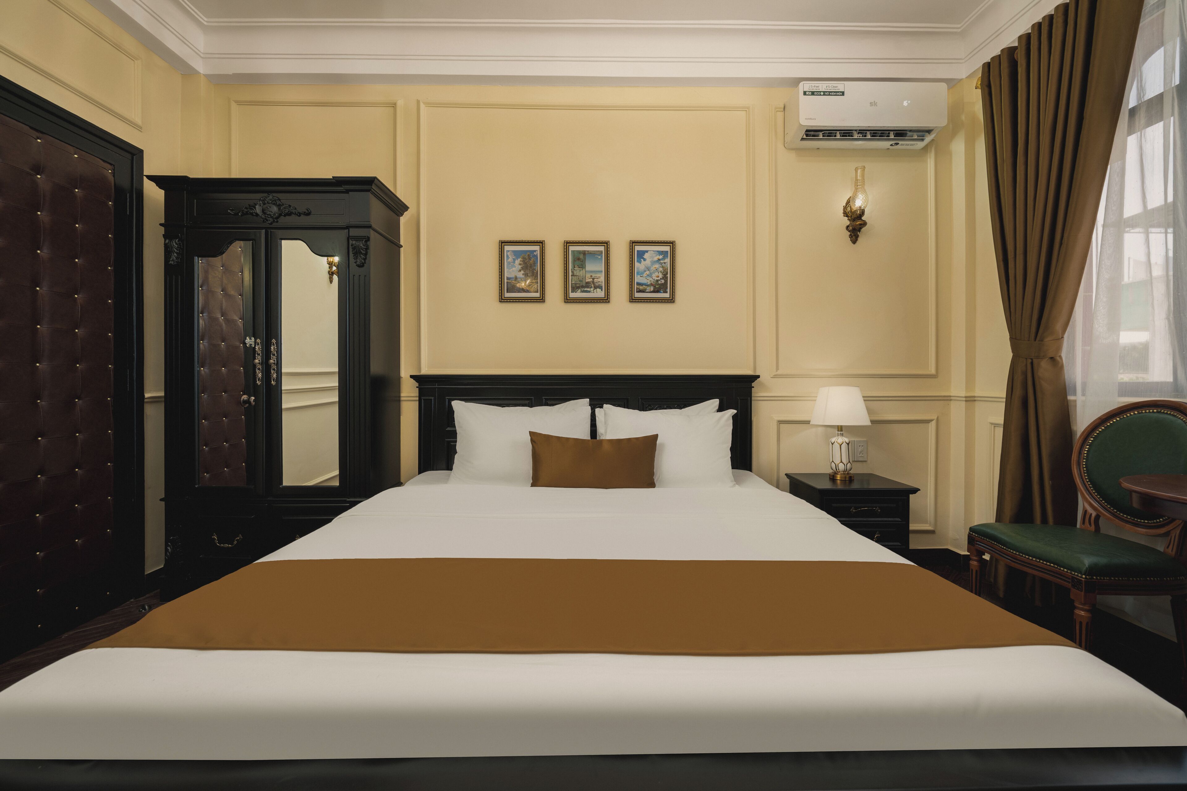 A hotel room with a large bed, a wardrobe, a mirror, a nightstand with a lamp, and a chair.