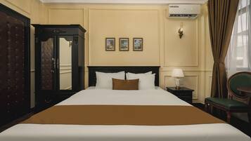 A hotel room with a large bed, a wardrobe, a mirror, a nightstand with a lamp, and a chair.