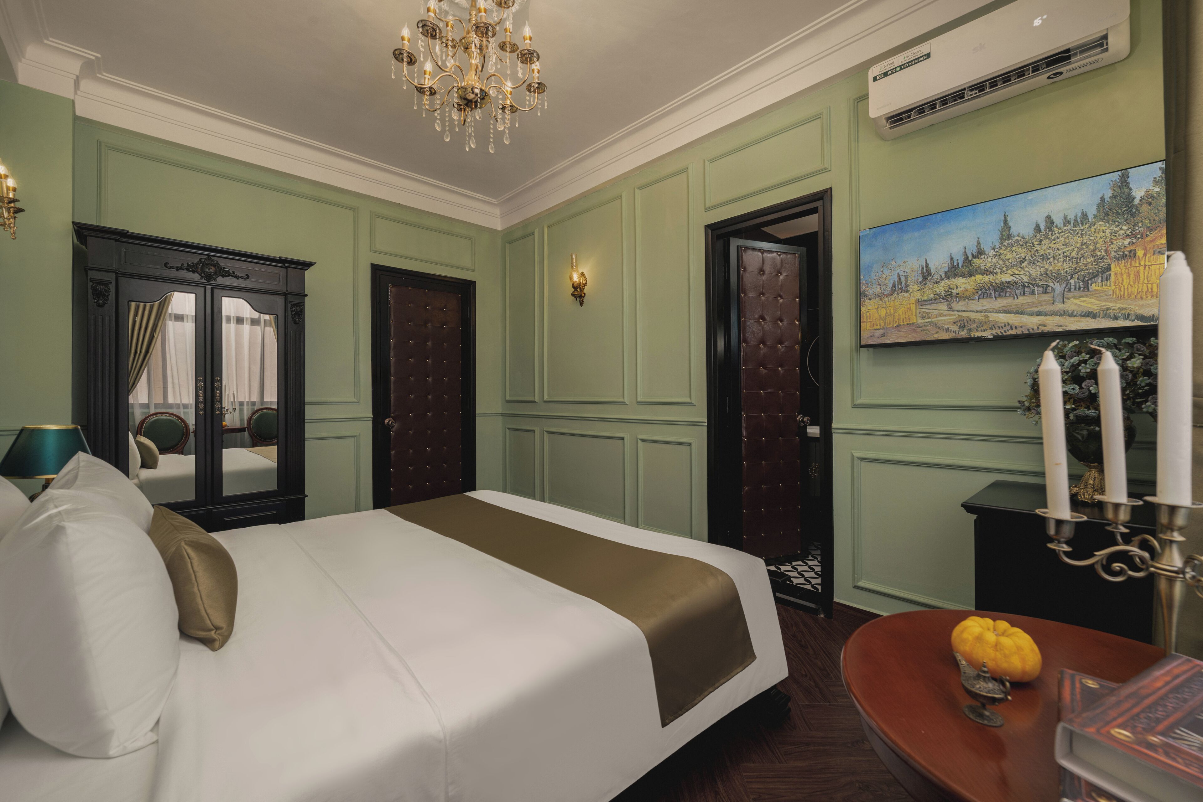 Habitación de hotel con una cama grande, una araña, un cuadro y una mesita con una vela.