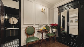 Una habitación con una mesa redonda de madera, dos sillones tapizados de verde, un espejo, una planta en maceta y un aparador de madera oscura con espejo.