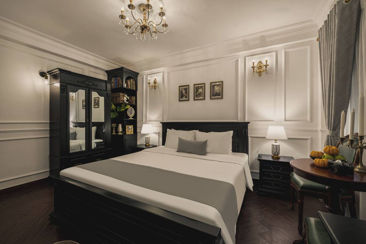 Una habitación de hotel con una cama grande, un tocador, una cómoda y un candelabro.