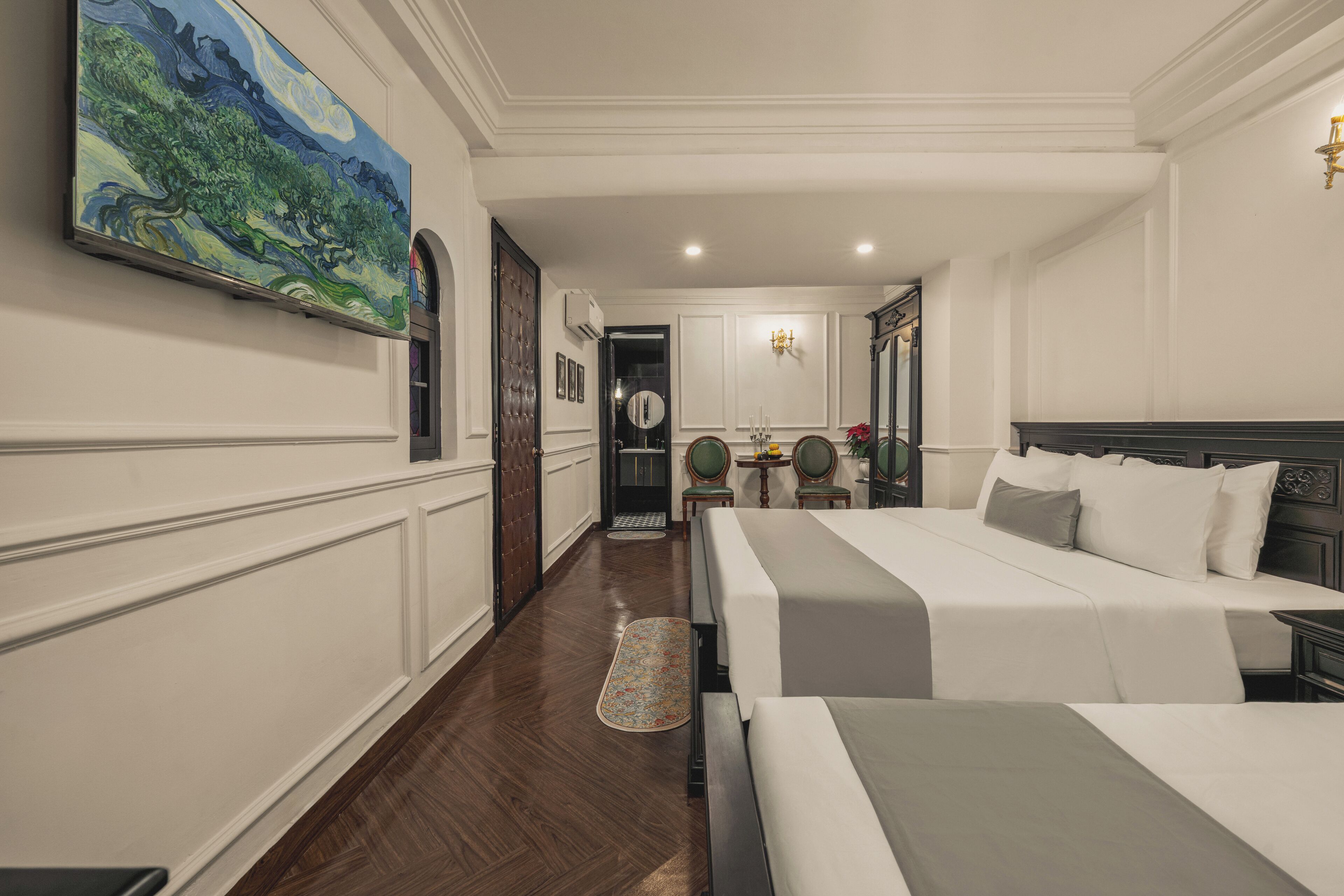 A hotel room with two beds, a large painting on the wall, a chandelier, and a wooden floor.