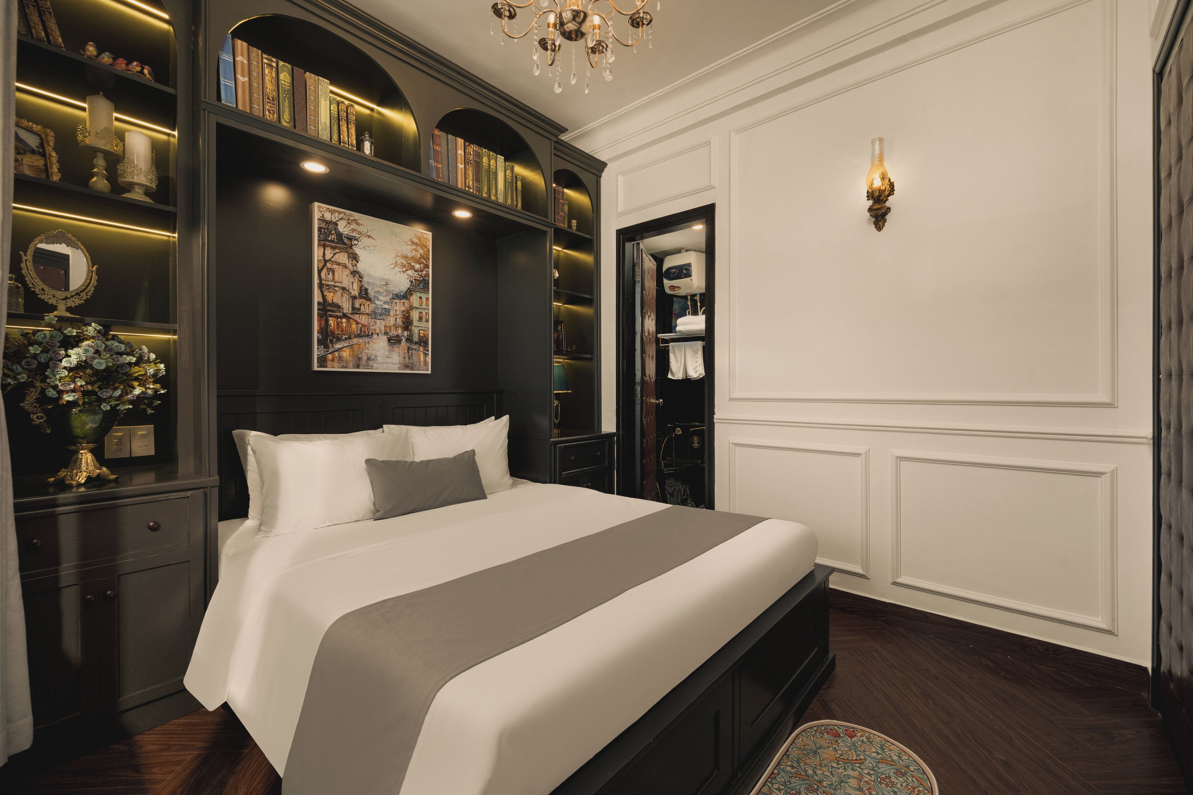 Un dormitorio con una cama grande, estanterías de madera oscura con libros, un cuadro y una araña.
