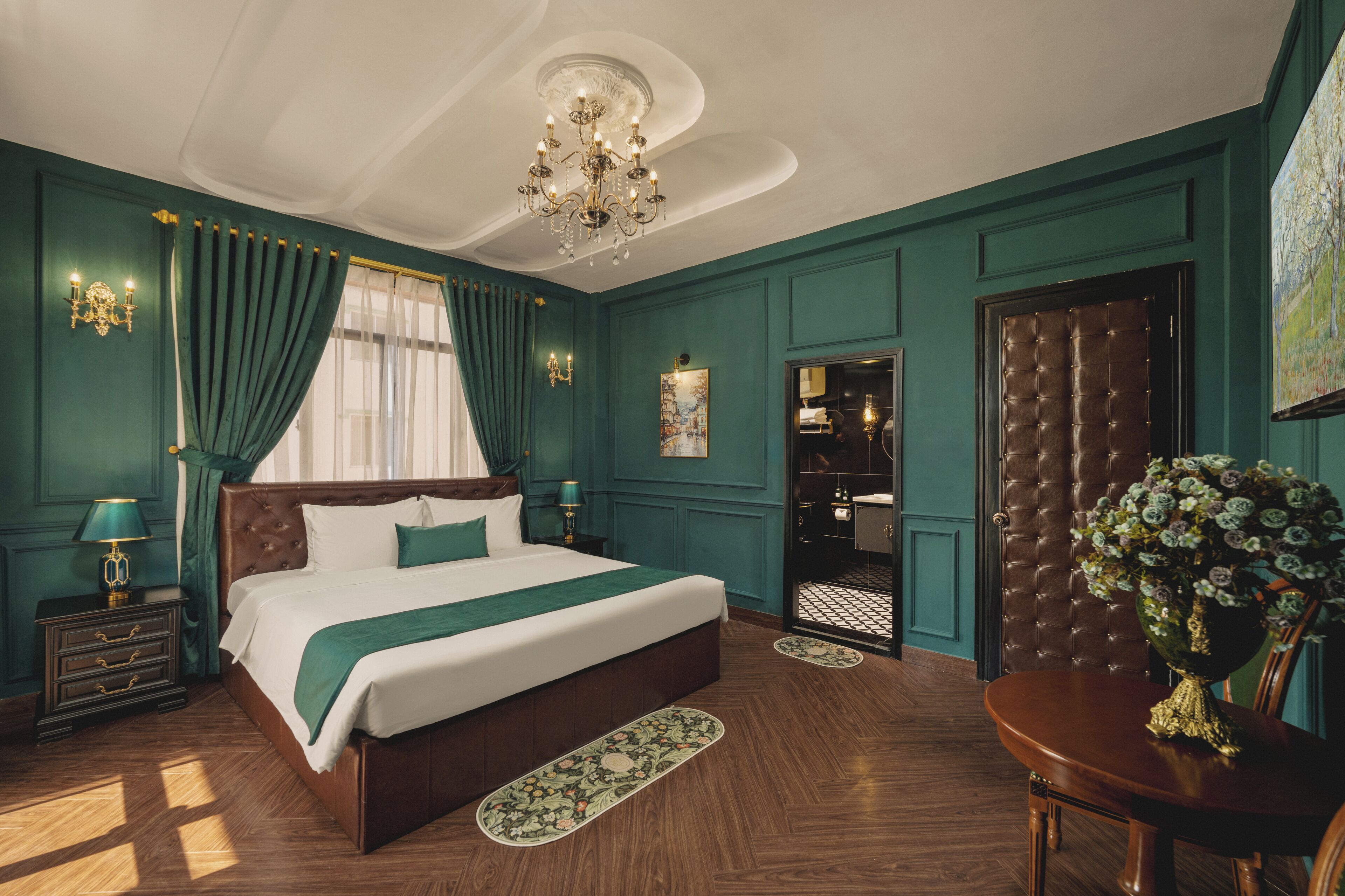 A large bed with a green bedspread, a chandelier, and a wooden floor.