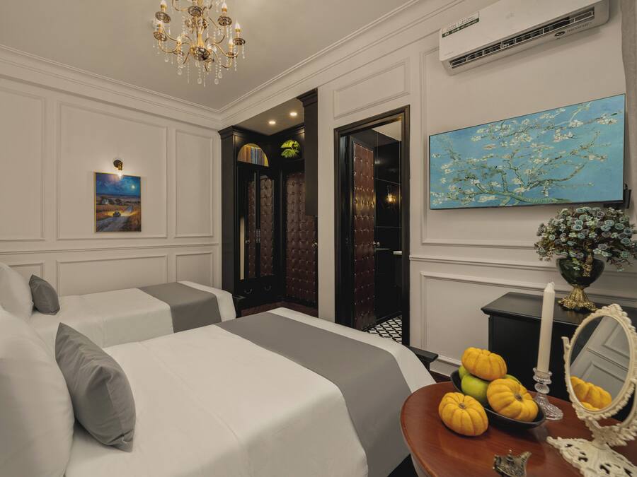 A hotel room with two beds, a chandelier, a painting, a mirror, and a vase with flowers.