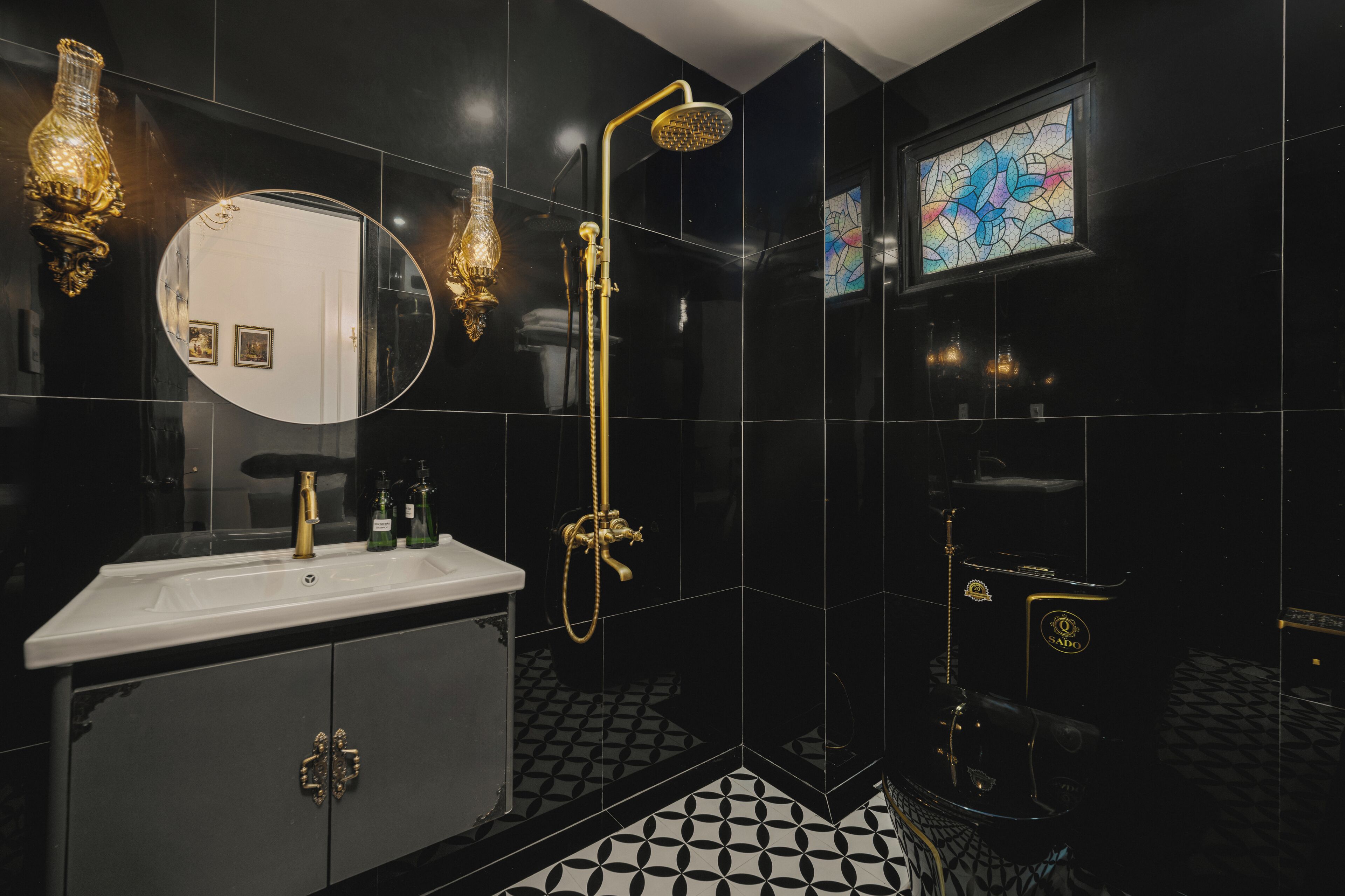 Une salle de bain moderne avec un carrelage noir et blanc, un lavabo blanc agrémenté de robinetterie dorée, une pomme de douche dorée et un grand miroir.