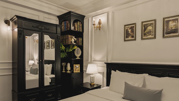 Una habitación de hotel con una cama grande, un armario de madera oscura, una mesita de noche con lámpara y cuadros en la pared.