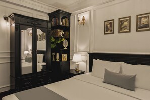 A hotel room with a large bed, a dark wooden wardrobe, a nightstand with a lamp, and framed pictures on the wall.