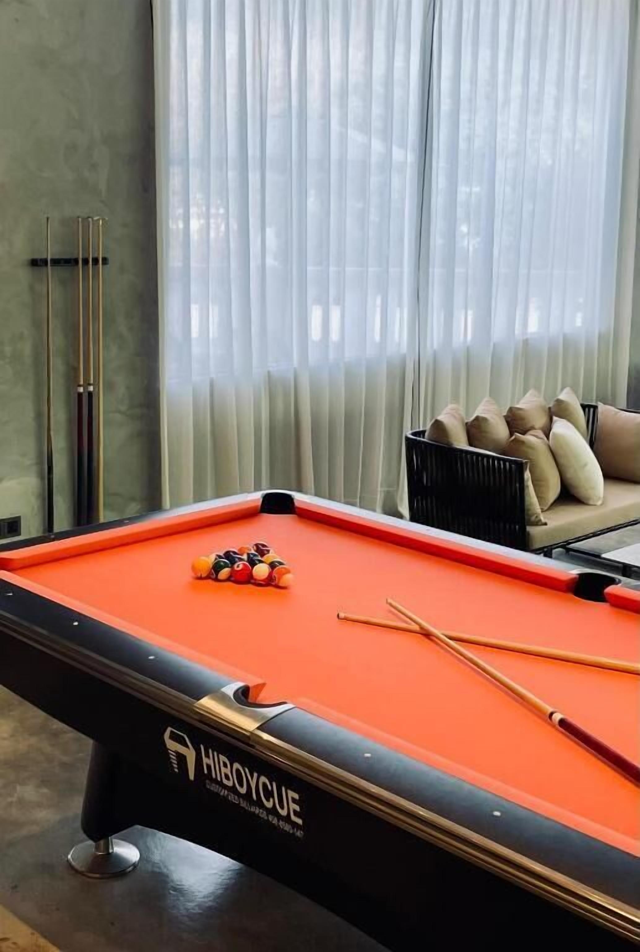 A pool table with balls and cues, a sofa with cushions, and a window with curtains.