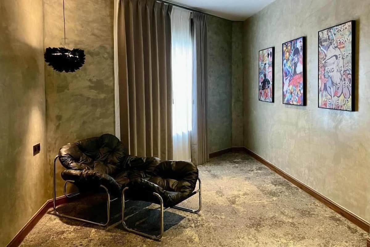 A hallway with a leather chair, a large window with curtains, and three abstract paintings on the wall.
