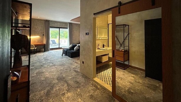 A spacious living area with a large window, a sofa, and a coffee table. There is a sliding door leading to a bathroom with a sink and mirror. - BaBa Boutique House Langkawi (Langkawi)