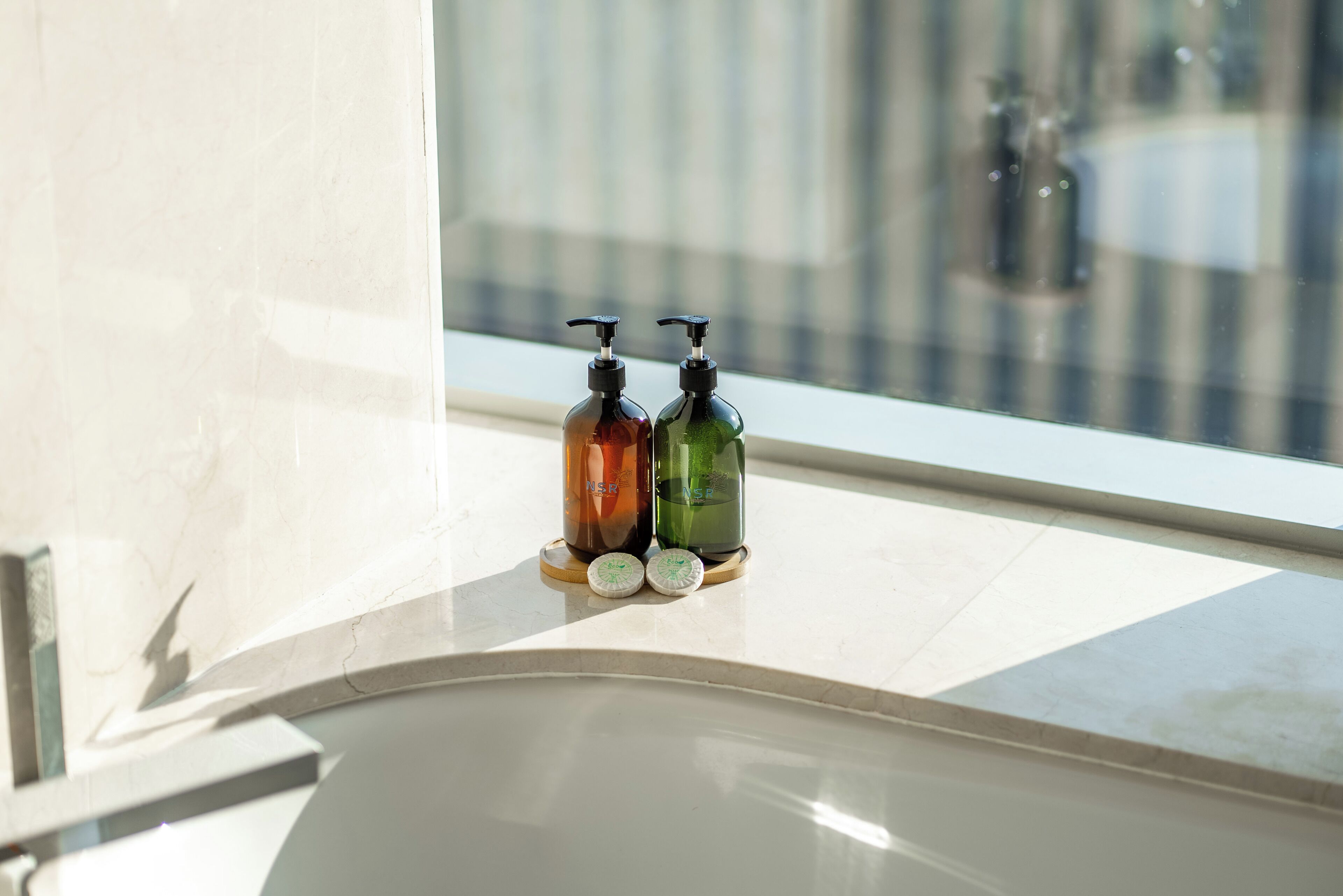 Dos dispensadores de jabón sobre una encimera de baño cerca de una ventana.