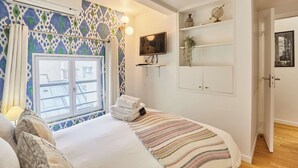 Ein Schlafzimmer mit einem Bett, einem Fenster mit Vorhängen, einem Fernseher an der Wand und einem Regal mit Dekoration.