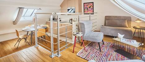 A loft-style room with a dining area, a sofa, a small table, and a window with curtains.