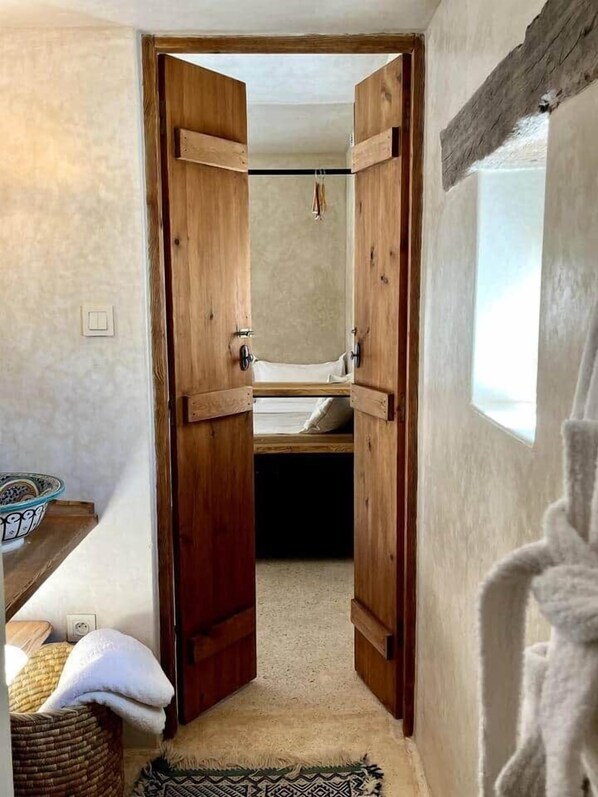 A narrow hallway with wooden doors leading to a bedroom.