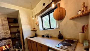 A cozy kitchen with a brick fireplace, wooden cabinets, a stove, and hanging light fixtures. - The Gate House Studio Sidi Kaouki (Douar Iskoha)
