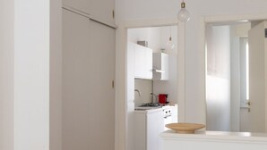 A compact kitchen with white cabinets, a stove, and a hanging light fixture.