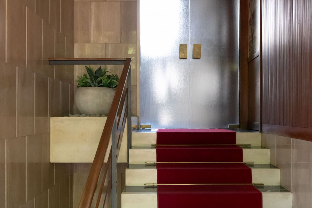 En trappe med rødt tæppe, en plantekasse med grønne planter og en metalforet elevatordør.