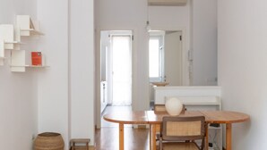 A modern, minimalist dining area with a round wooden table, wicker chairs, and a white vase.