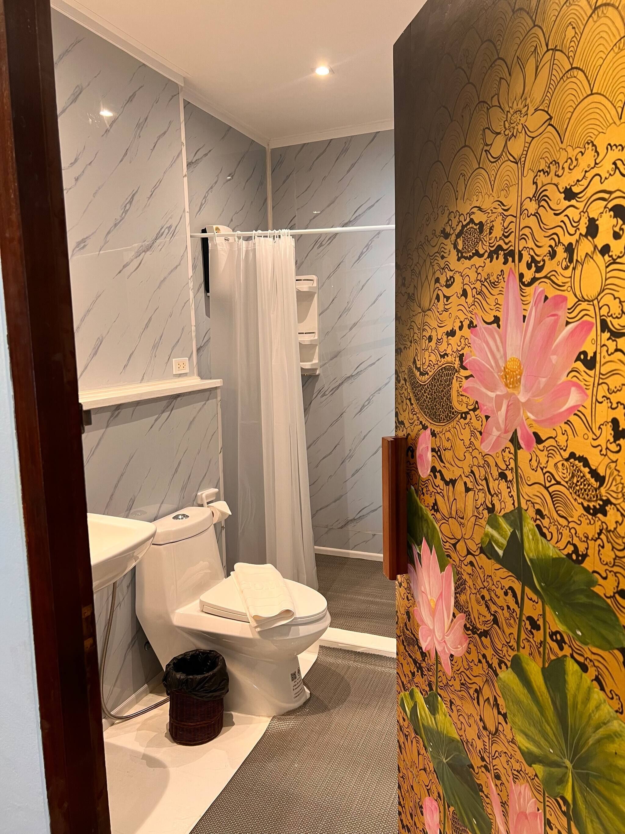 Un baño con inodoro, ducha y un revestimiento decorativo con motivos florales.