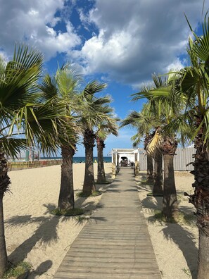 A wooden pathway leading to a beach area with palm trees and a gazebo.
